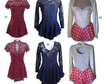 May include: Four figure skating dresses in different styles and colors. The dresses are all short and have lace detailing. The first dress is burgundy with short sleeves, the second and third dresses are blue with long sleeves, and the fourth dress is white with red polka dots and long sleeves.