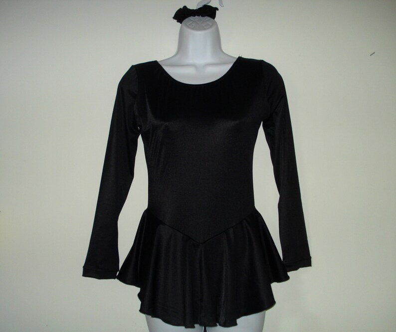 May include: Black long-sleeved leotard with a flared skirt and a matching scrunchie. The leotard has a scoop neckline and a fitted bodice. The skirt flares out from the waist. The scrunchie is on a mannequin head.