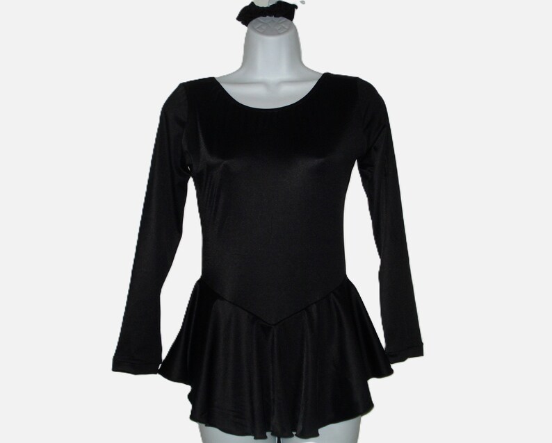 May include: A black long-sleeved leotard with a flared skirt and a matching scrunchie. The leotard has a scoop neckline and a fitted bodice. The skirt flares out from the waist. The scrunchie is at the top of the mannequin head.