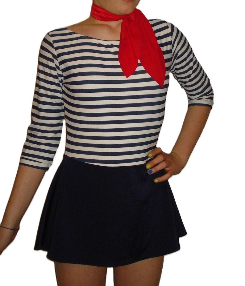May include: A nautical-themed outfit featuring a striped long-sleeve top in navy and white, paired with a navy skirt. A red scarf is tied around the neck. The outfit is a classic, timeless style.