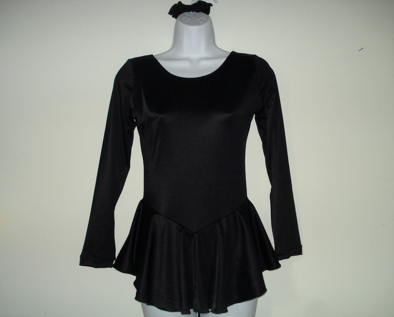 May include: A black long-sleeved leotard with a flared skirt and a matching scrunchie. The leotard has a scoop neckline and a fitted bodice. The skirt flares out from the waist. The scrunchie is on a mannequin head.