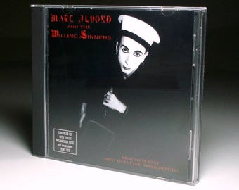 May include: CD case for "Mother Fist and Her Five Daughters" by Marc Almond and The Willing Sinners. The cover is a monochrome image of a person in a sailor hat. Text includes "Enhanced CD with videos" and song titles, in a clear plastic case.