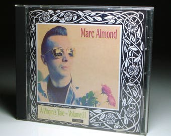 May include: A CD case for Marc Almond's album "A Virgin's Tale - Volume II". The cover art features a man in sunglasses, with the artist's name in red. The case is framed by a decorative black and white border.