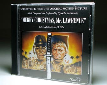 May include: CD case for the soundtrack of "Merry Christmas, Mr. Lawrence," a Nagisa Oshima film. The cover features two men's faces, a sword, and the film's title. The Milan logo is at the bottom.