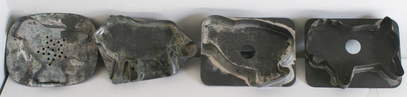 May include: Four vintage metal cookie cutters in the shapes of a bird, a cow, a pig, and a dog. The cutters are made of a dark gray metal and have a slightly worn appearance.