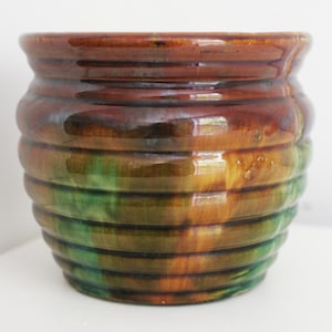 May include: A glazed ceramic planter with a ribbed design. The planter features a gradient of colors, including brown, green, and yellow. The glossy finish enhances the colors. This decorative pot is suitable for indoor or outdoor use.