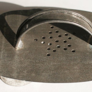 May include: A vintage metal cookie cutter shaped like a heart with a handle. The cutter has a pattern of small holes on the surface.