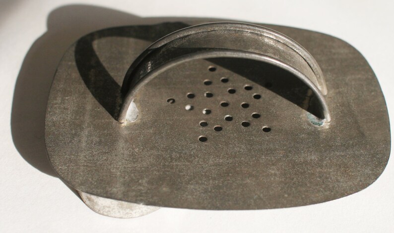 May include: A vintage metal cookie cutter shaped like a heart with a handle. The cutter has a pattern of small holes on the surface.