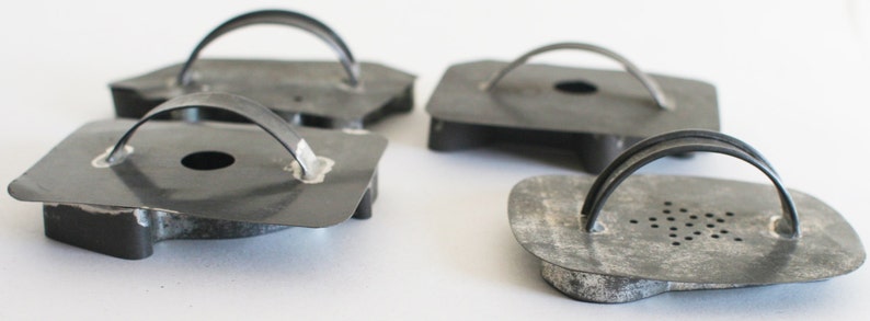 May include: Four vintage metal cookie cutters with handles. The cutters are shaped like a heart, a circle, a star, and a flower. The cutters are made of dark gray metal and have a rustic look.