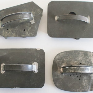 May include: Four vintage metal cookie cutters with handles. The cutters are in various shapes, including a rectangle, a square, and a freeform shape. The cutters are all gray and have a worn, rustic look.