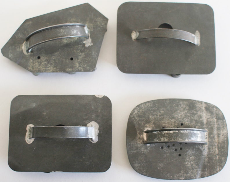 May include: Four vintage metal cookie cutters with handles. The cutters are in various shapes, including a rectangle, a square, and a freeform shape. The cutters are all gray and have a worn, rustic look.