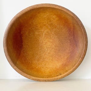 May include: A round wooden bowl with a natural light brown finish, featuring a visible grain pattern and numerous fine surface scratches throughout the interior, showcasing a smooth, curved rim and a deep, concave basin for holding items.