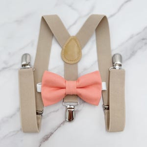 May include: A set of beige suspenders with a coral bow tie. The suspenders have a leather detail on the back.