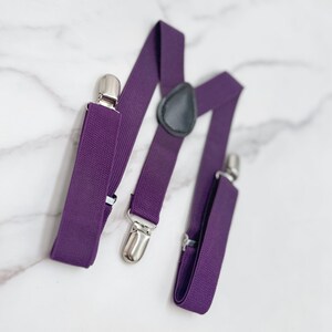 May include: Purple suspenders with silver clips and a black leather adjustable strap.