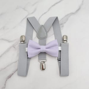 以下が含まれることがあります： シルバーのクリップとラベンダー色の蝶ネクタイが付いたグレーのサスペンダー。蝶ネクタイは布製で、クラシックな形をしています。