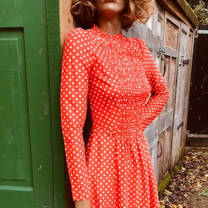 May include: A red dress with white polka dots and a high neck. The dress has long sleeves and a fitted bodice. The skirt is full and flows out from the waist.