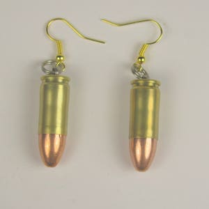 May include: A pair of gold bullet earrings with copper tips. The earrings are made from real bullet casings and have a gold hook.