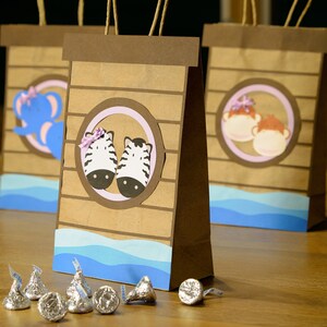 May include: Brown paper gift bags with animal-themed cutouts, including zebras, elephants, and monkeys. Each bag has a blue wave design at the bottom and a brown handle. Silver chocolate candies are scattered in front of the bags.