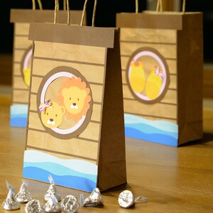 May include: Brown paper gift bags with a light blue wave design at the bottom. Each bag features a circular design with cartoon animals. Silver foil-wrapped chocolate candies are scattered in front of the bags.