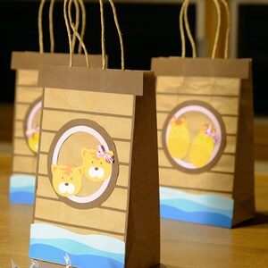 May include: Brown paper gift bags with a decorative design. Each bag features a circular design with cartoon tiger faces and a blue wave pattern at the bottom. Several foil-wrapped chocolate candies are in front of the bags.