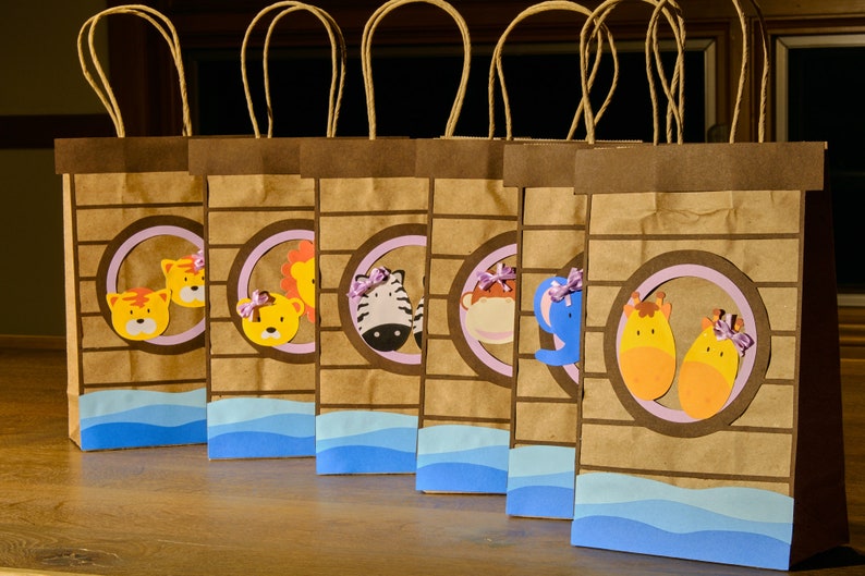 May include: Six brown paper gift bags with animal-themed cutouts. Each bag features a different animal, including a tiger, lion, zebra, monkey, elephant, and giraffe. The bags have light blue wave accents and brown handles.