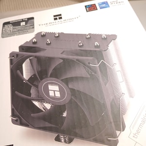 May include: A black Thermalright CPU cooler with a fan and heat sink fins. The cooler is on a white box with the Thermalright logo and product information. The fan has a circular logo in the center.
