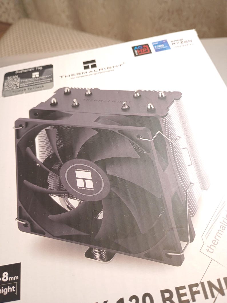 May include: A black Thermalright CPU cooler with a fan and heat sink fins. The cooler is on a white box with the Thermalright logo and product information. The fan has a circular logo in the center.