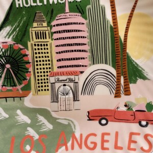 May include: A decorative plate featuring a colorful illustration of Los Angeles landmarks. The plate includes the Hollywood sign, Capitol Records, a Ferris wheel, and a red convertible car. The words "HOLLYWOOD" and "LOS ANGELES" are prominently displayed.