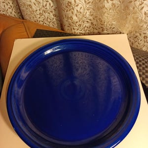 May include: A large, round, cobalt blue ceramic serving platter. The platter has a slightly raised rim and a smooth, glossy finish.