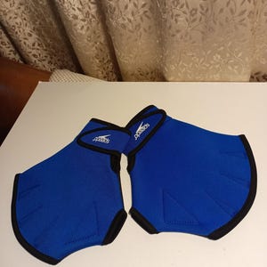 May include: A pair of blue Speedo swim training hand paddles. The paddles are made of a flexible material with black trim and a Speedo logo. They are designed to enhance swimming technique and strength.