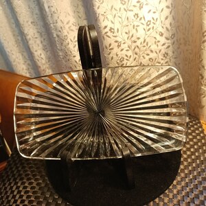 May include: A clear glass serving dish with a sunburst pattern. The dish is on a black stand.