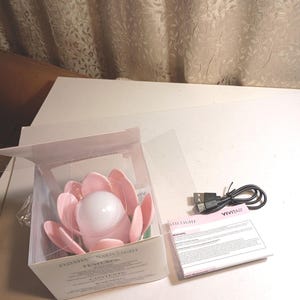 May include: A pink lotus-shaped floating bath light inside a clear plastic box with white packaging. The set includes a black USB charging cable and a white Vivitar instruction manual with warranty information printed on the front.