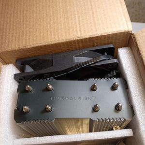 May include: A new computer CPU cooler, featuring a black fan and a silver heat sink with the text "THERMALRIGHT" printed on it. The cooler is packaged in a cardboard box with protective foam.