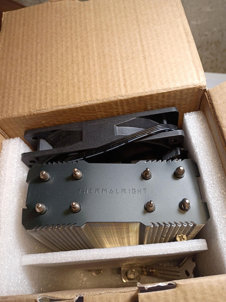May include: A new computer CPU cooler, featuring a black fan and a silver heat sink with the text "THERMALRIGHT" printed on it. The cooler is packaged in a cardboard box with protective foam.