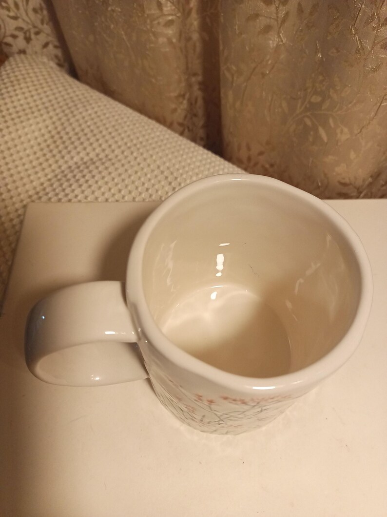 Puede incluir: Taza de cer&aacute;mica blanca con asa redondeada. La taza tiene un dise&ntilde;o floral en rosa y verde. El interior de la taza es blanco. La taza est&aacute; sobre una superficie blanca.