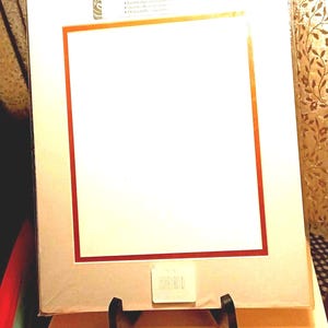 May include: A white acid-free print mat with a red and gold border, displayed on a black easel. The mat has a large rectangular opening and is packaged in clear plastic. The text "ACID FREE PRINT" is visible.