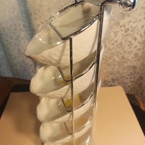 May include: A set of five white ceramic bowls with a textured finish, stacked on a chrome stand with rounded ends. The bowls are nested inside each other and are wrapped in plastic.