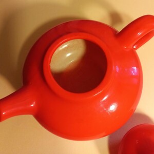 May include: A bright red ceramic teapot with a rounded body and a single handle. The teapot has a smooth, glossy finish.