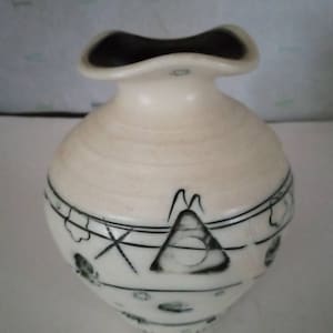 May include: A white ceramic vase with a black and white geometric design. The vase has a wide mouth and a rounded body.