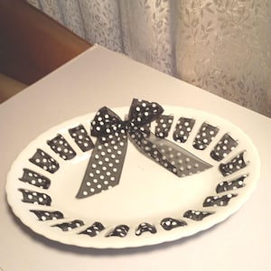 May include: White oval serving platter with a black and white polka dot bow and matching polka dot accents around the rim. The bow is centered on the platter, adding a decorative touch to the serving dish.