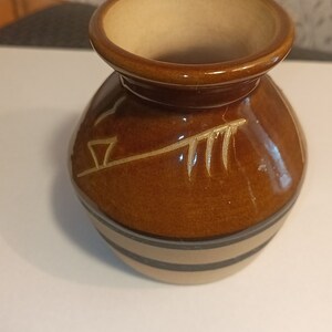 May include: A small, brown ceramic vase with a decorative design. The vase has a wide mouth and a narrow base.