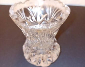May include: A clear glass vase with a decorative, cut-glass design. The vase has a wide, flared opening and a narrow base.