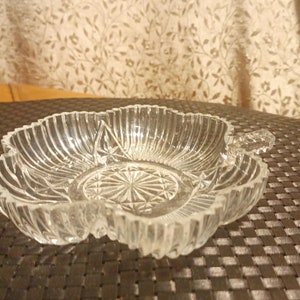 May include: A clear glass dish with a decorative design. The dish has a scalloped edge and a handle on one side.