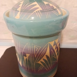 May include: A blue ceramic jar with a lid, featuring a geometric pattern in shades of blue, purple, and white.