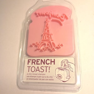 May include: Pink bread stamper in a clear plastic package. The stamper features an Eiffel Tower design and the words "French Toast!". The packaging also includes the text "a chic bread stamper".