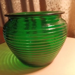 May include: A green glass vase with a ribbed design. The vase is round and has a wide opening.