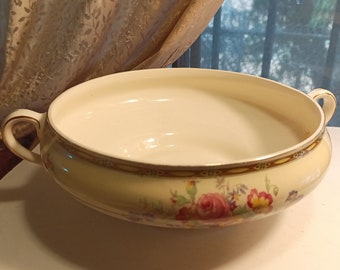 May include: A white ceramic serving bowl with a gold rim and floral pattern. The bowl has two handles and is decorated with pink, yellow, and green flowers.
