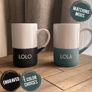 May include: Two ceramic mugs with speckled white upper halves and solid lower halves in black and teal. The black mug features the engraved name LOLO, and the teal mug features the engraved name LOLA. Text overlays state MATCHING MUGS and ENGRAVED 4 COLOR CHOICES.