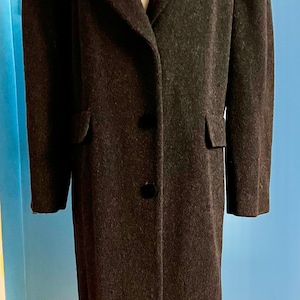 May include: A long, dark gray wool coat with a black velvet collar. The coat has a single-breasted closure with four black buttons and two flap pockets.