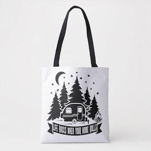 Può includere: Una borsa tote bianca con manici neri e un design nero. Il design presenta un camper, alberi, una luna crescente, stelle e un falò. Il testo sulla borsa recita "Life rocks when your home rolls."